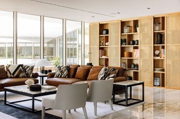 Light and stylish living room with brown leather sofas, a large wooden bookshelf, and floor-to-ceiling white windows allowing natural light to fill the space - Reynaers